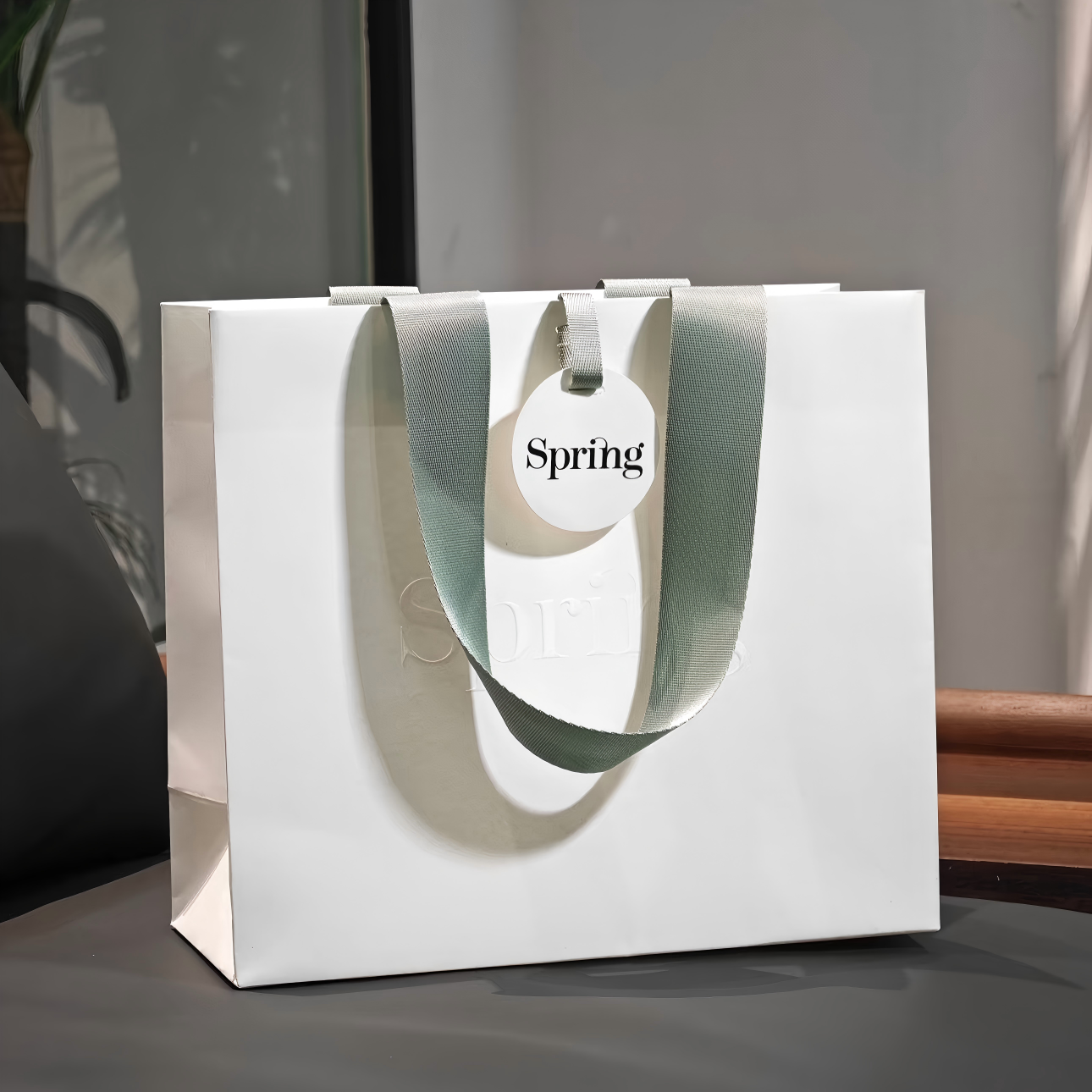 White gift paper bag with wide sage ribbon handles and a round tag