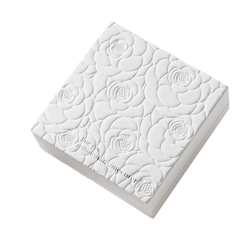 White gift-box lid with raised floral relief across the surface