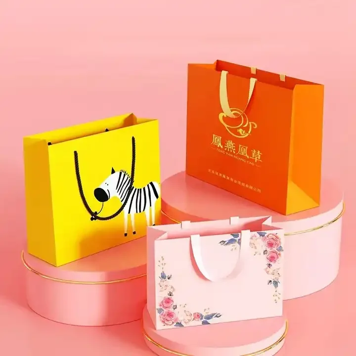 Yellow, orange and pink printed paper gift bags with cord and ribbon handles on a pink display