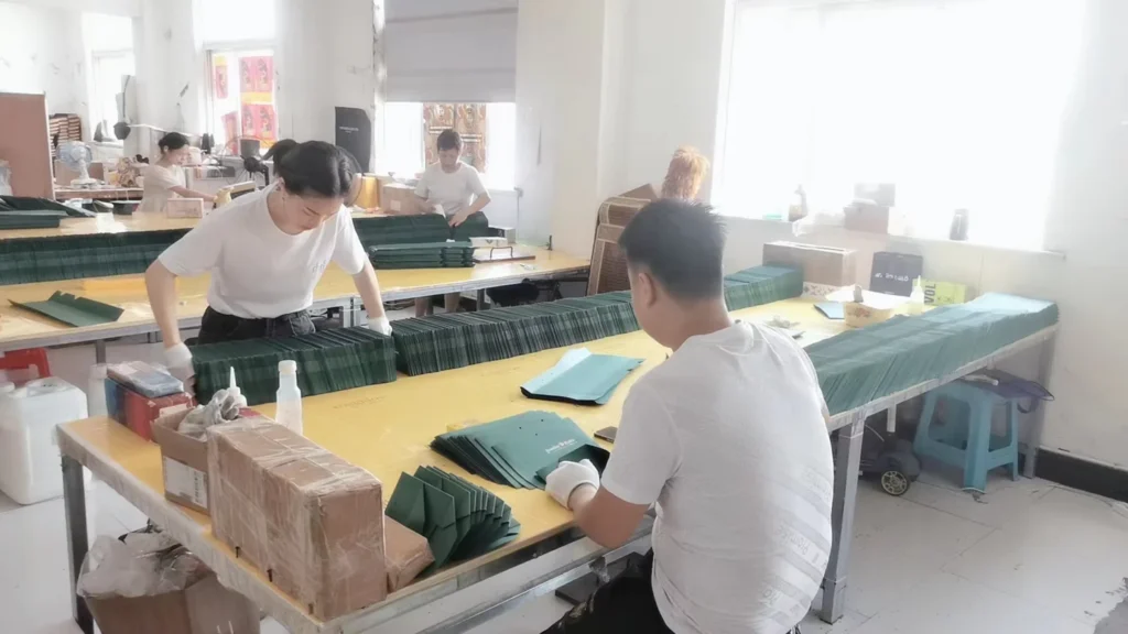 Workers assembling dark green paper bags at production tables